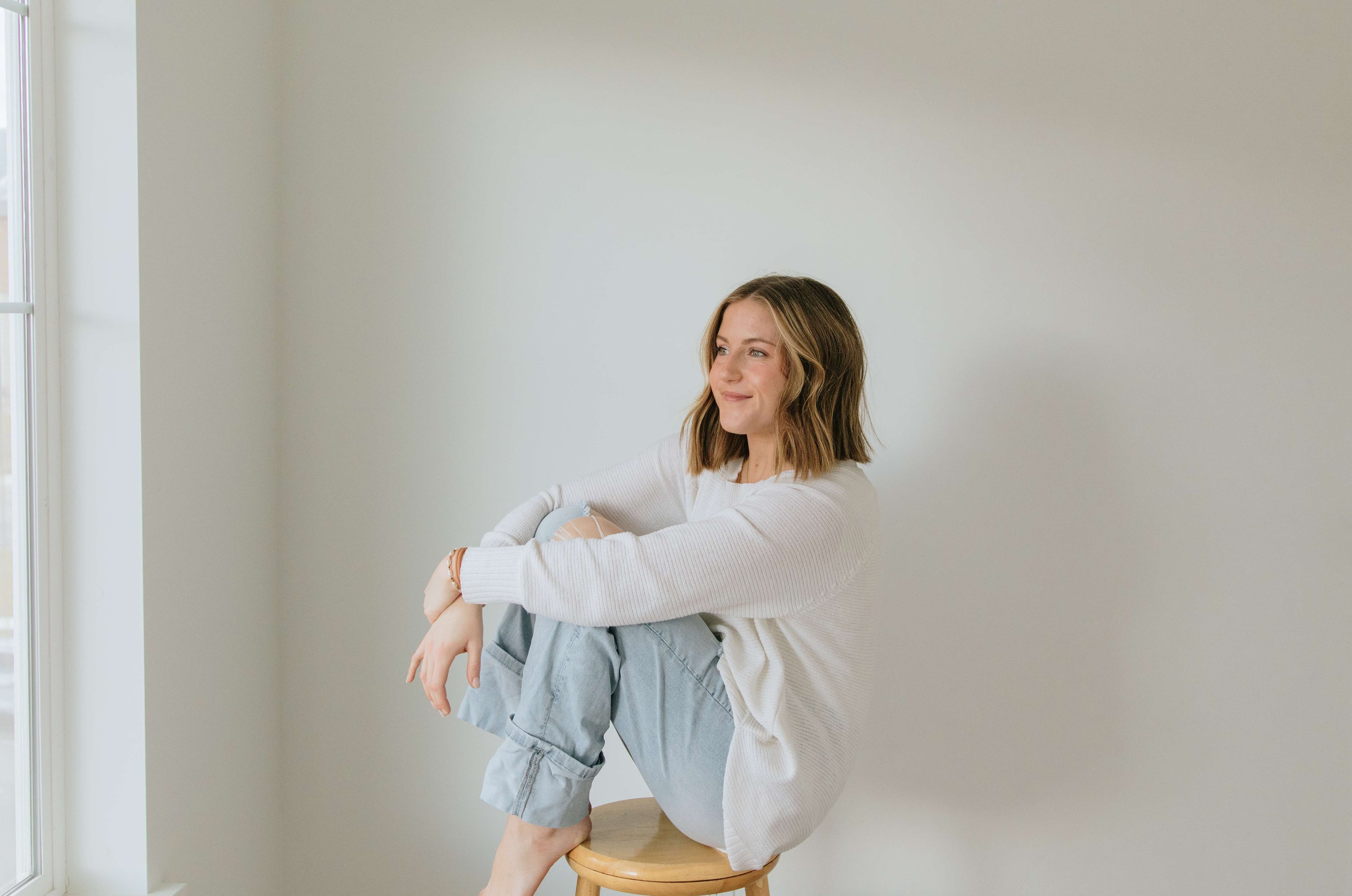 Kait, the business owner, seated in a bright studio wearing a white textured top and striped trousers