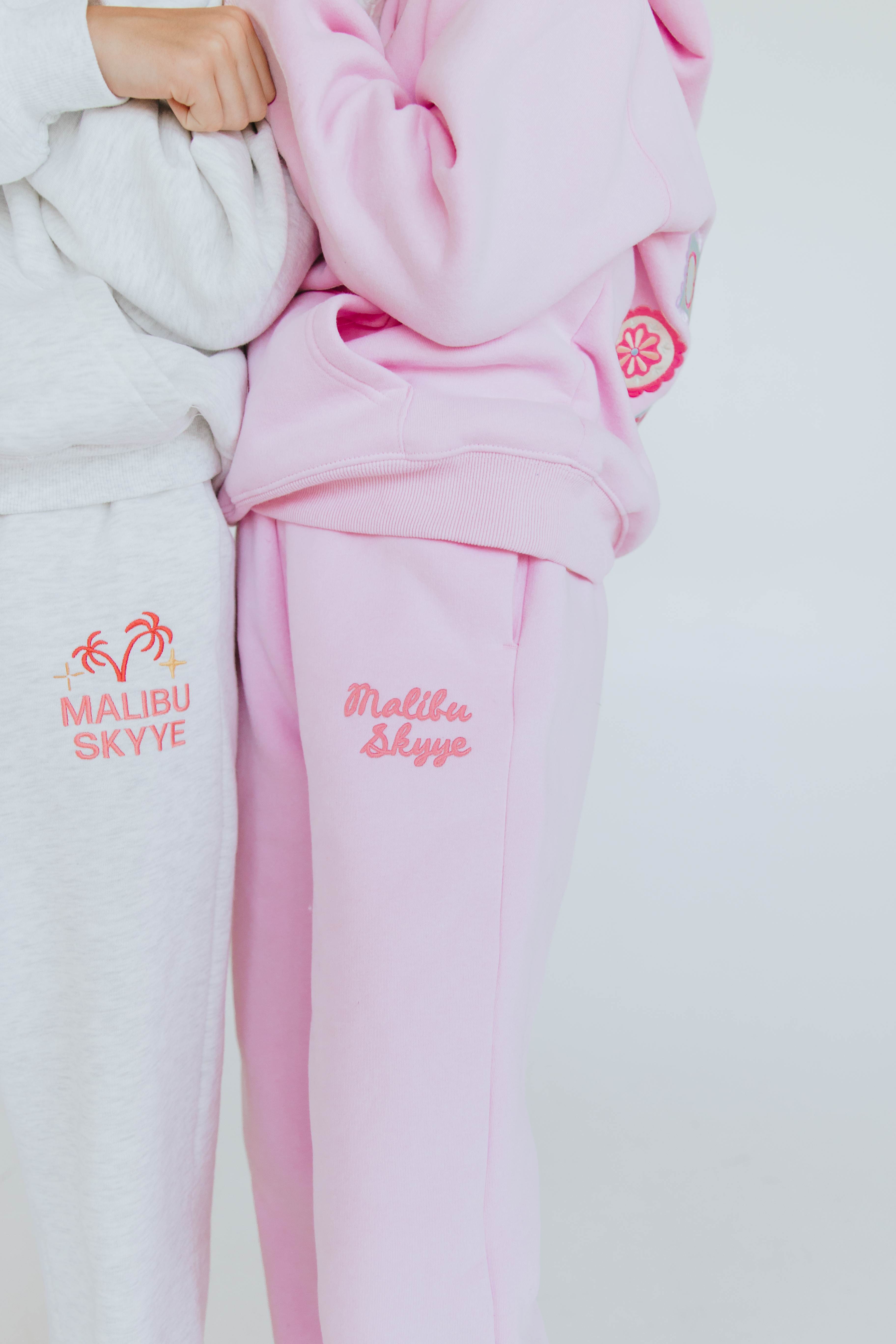 Close-up of embroidered Malibu Skyye branding on gray and pink sweatsuits.