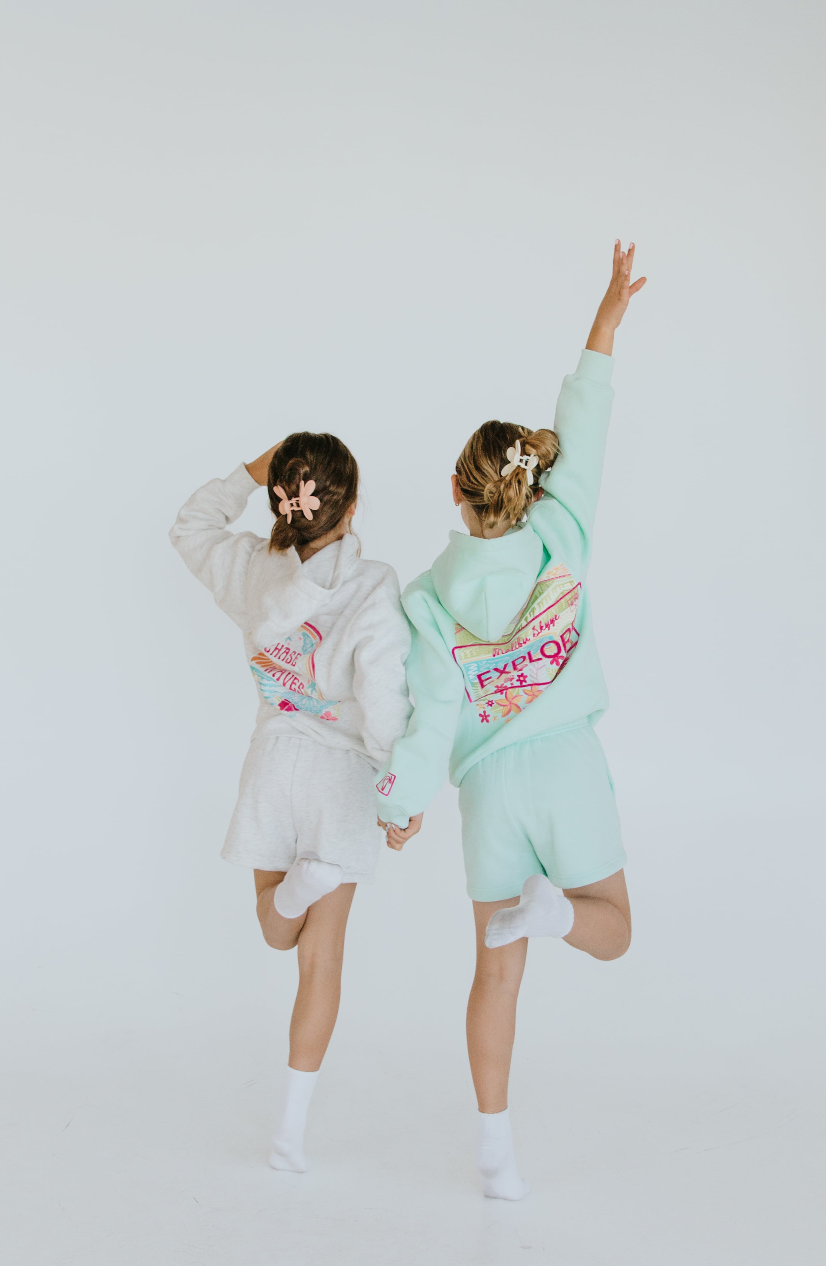 Two models showing the colorful back designs of Malibu Skyye outfits in a bright studio.